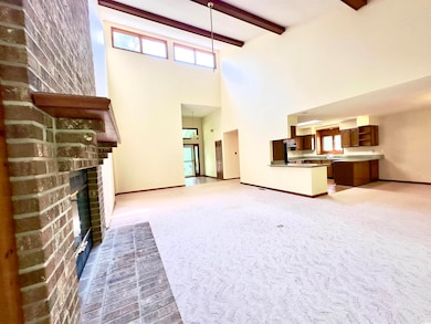 Unfurnished living room with a high ceiling, a brick fireplace, light colored carpet, and beamed ceiling