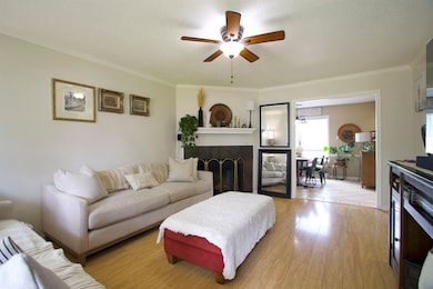 Living area with a ceiling fan, ornamental molding, a fireplace, light wood finished floors, and a textured ceiling