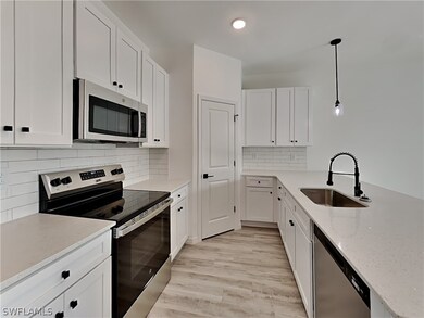 This is a picture of a previously completed home. Kitchen with tasteful backsplash, light hardwood / wood-style floors, appliances with stainless steel finishes, decorative light fixtures, and sink