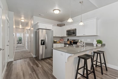 Kitchen featuring stainless steel appliances, white cabinets, pendant lighting, peninsula, and LVP