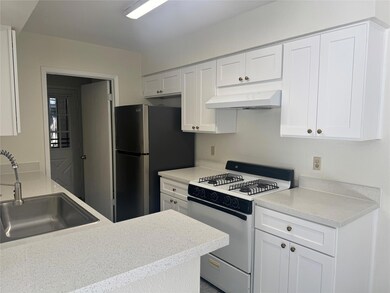 Kitchen featuring white gas stove, white cabinets, under cabinet range hood, freestanding refrigerator, and light stone countertops