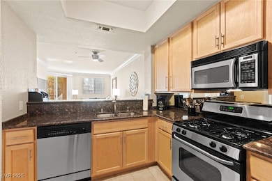 Kitchen featuring stainless steel appliances, light brown cabinets, dark stone counters, light tile patterned flooring, and a textured wall