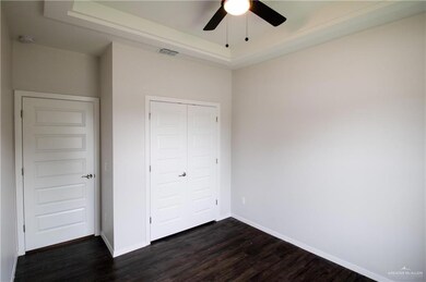 Unfurnished bedroom with dark wood-type flooring, a raised ceiling, a closet, and ceiling fan