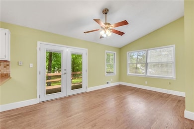 Unfurnished room featuring french doors, light wood-style floors, ceiling fan, lofted ceiling, and baseboards