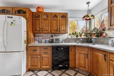 Kitchen with freestanding refrigerator, brown cabinetry, inlaid floor details, and black dishwasher