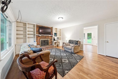 Living room featuring a textured ceiling, wood finished floors, a brick fireplace, and built in features
