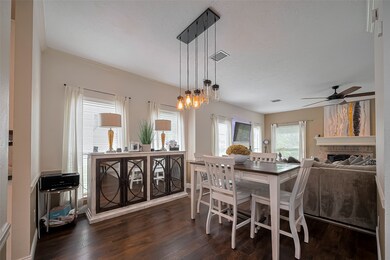 Bright and inviting dining area with hardwood floors, modern pendant lighting, and large windows. The space flows into a cozy living room featuring a ceiling fan and fireplace, creating a perfect setting for entertaining or relaxing.