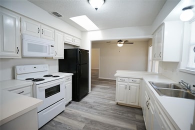 Kitchen featuring white appliances, white cabinets, light countertops, light wood-type flooring, and a textured ceiling