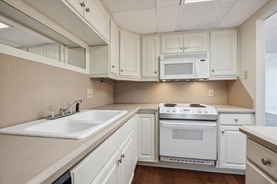 Kitchen featuring white appliances, a paneled ceiling, light countertops, dark wood finished floors, and white cabinets