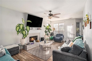 Living area featuring wood finished floors, a textured ceiling, a fireplace, and a ceiling fan