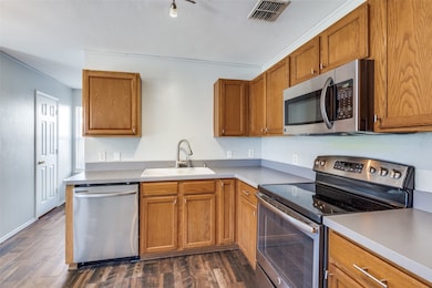 Kitchen featuring appliances with stainless steel finishes, brown cabinets, dark wood-style floors, and light countertops