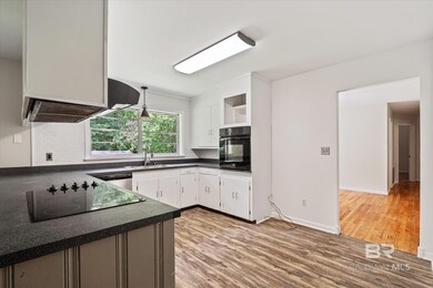 Kitchen featuring white cabinetry, black appliances, hanging light fixtures, light hardwood / wood-style flooring, and backsplash