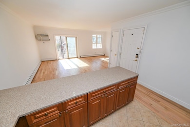 Kitchen featuring light wood finished floors, a baseboard radiator, crown molding, brown cabinets, and light stone countertops