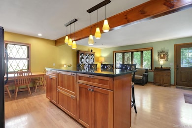 Kitchen featuring beam ceiling, a kitchen bar, pendant lighting, brown cabinetry, and light wood finished floors