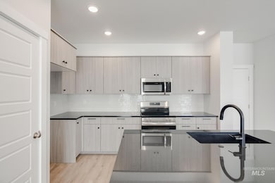 Kitchen featuring appliances with stainless steel finishes, backsplash, light wood finished floors, modern cabinets, and dark stone countertops