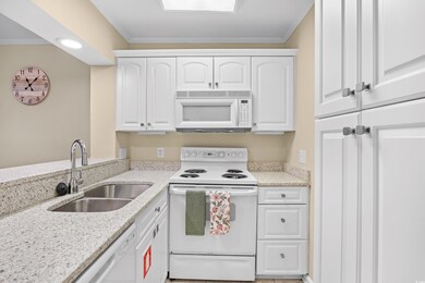 Kitchen featuring white appliances, white cabinets, light stone counters, and ornamental molding