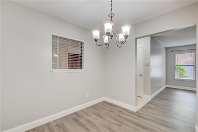 Spare room with a chandelier, light wood finished floors, a textured ceiling, and baseboards