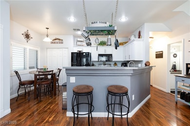 Kitchen with white cabinets, dark wood finished floors, black appliances, a peninsula, and decorative light fixtures
