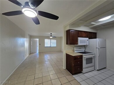 Kitchen with white appliances, light countertops, dark brown cabinets, light tile patterned floors, and open floor plan