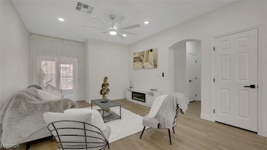 Living room with a glass covered fireplace, light wood-style flooring, recessed lighting, arched walkways, and a ceiling fan
