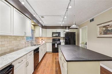 Kitchen with black appliances, wood-type flooring, backsplash, a kitchen island, and white cabinets
