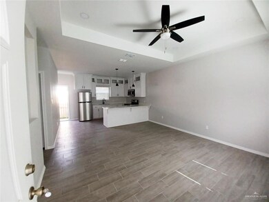 Unfurnished living room with a tray ceiling, a ceiling fan, baseboards, and dark wood-style floors