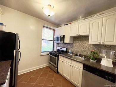 Kitchen featuring appliances with stainless steel finishes, dark tile patterned flooring, decorative backsplash, and white cabinets