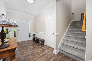 Foyer with wood finished floors, stairway, and crown molding
