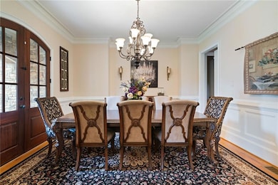 Dining area featuring a decorative wall, crown molding, a wainscoted wall, a chandelier, and french doors