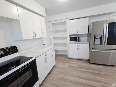 Kitchen featuring stainless steel appliances, light wood finished floors, open shelves, and white cabinetry