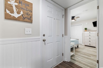 Doorway with wood finished floors, wainscoting, and a ceiling fan