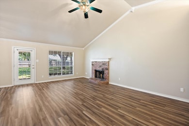 Living room with a fireplace, vaulted ceiling, crown molding, laminate flooring, view of back yard