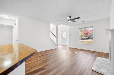 Unfurnished living room with dark wood finished floors, a textured ceiling, a ceiling fan, and stairway