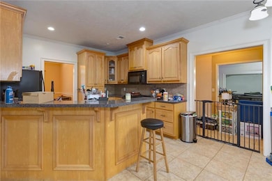Kitchen with black microwave, light tile patterned floors, a breakfast bar, glass insert cabinets, and decorative backsplash