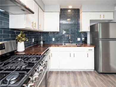 Kitchen featuring stainless steel appliances, under cabinet range hood, light wood-type flooring, tasteful backsplash, and white cabinets