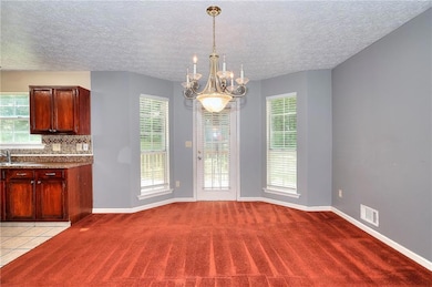 Unfurnished dining area featuring light carpet, a chandelier, and a textured ceiling