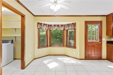 Unfurnished dining area with washer / dryer, a ceiling fan, crown molding, and light tile patterned floors