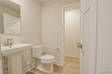 Half bath with toilet, a sink, baseboards, and wood finished floors