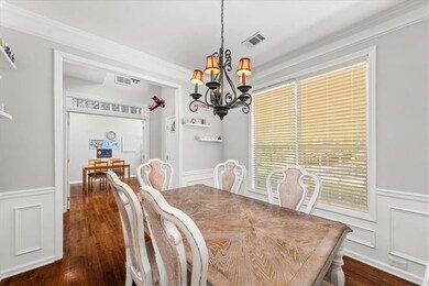 Dining area featuring a chandelier, wainscoting, a decorative wall, dark wood-type flooring, and ornamental molding
