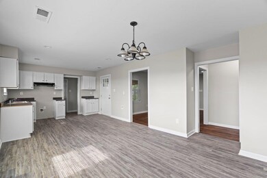 Kitchen featuring white cabinetry, a chandelier, light wood finished floors, under cabinet range hood, and decorative light fixtures