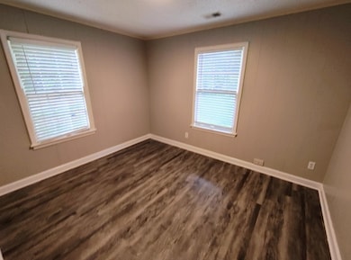 Spare room featuring dark wood-type flooring and baseboards