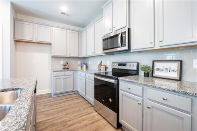 Kitchen featuring stainless steel appliances, light wood-type flooring, light stone countertops, and tasteful backsplash