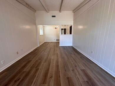 Empty room with dark wood-type flooring, beam ceiling, a chandelier, a textured ceiling, and wood walls