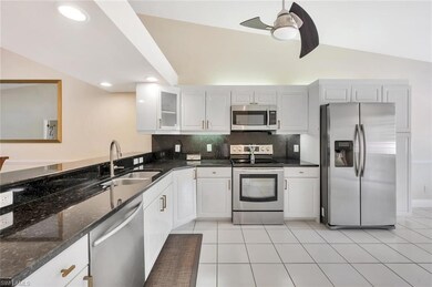 Kitchen with stainless steel appliances, ceiling fan, decorative backsplash, glass insert cabinets, and dark stone counters