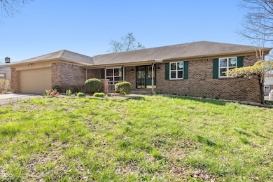 single story home with a shingled roof, an attached garage, concrete driveway, brick siding, and a front lawn