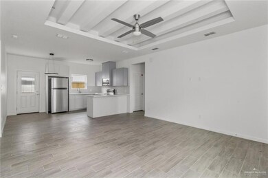 Unfurnished living room with a tray ceiling, beam ceiling, a ceiling fan, and light wood-type flooring