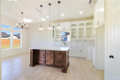 Kitchen featuring glass insert cabinets, white cabinetry, tasteful backsplash, a kitchen island, and hanging light fixtures