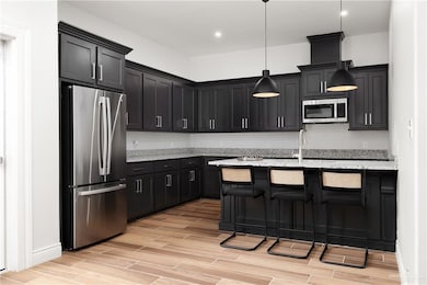 Kitchen with a breakfast bar area, stainless steel appliances, dark cabinets, light stone countertops, and recessed lighting