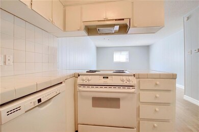 Kitchen featuring tile counters, white appliances, exhaust hood, and cream cabinetry