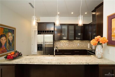 Kitchen featuring kitchen peninsula, light stone countertops, hanging light fixtures, stainless steel refrigerator with ice dispenser, and backsplash